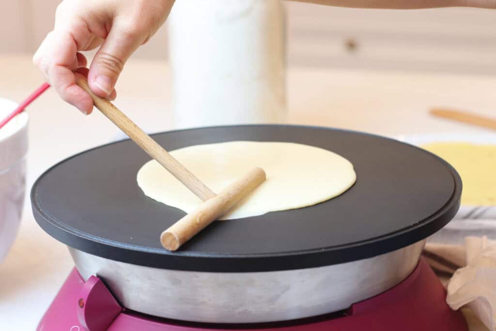 Delicious French crêpe being cooked on a pancake maker, showcasing French cuisine and breakfast favorite. Hand pressing the batter for authentic homemade French-style pancakes.