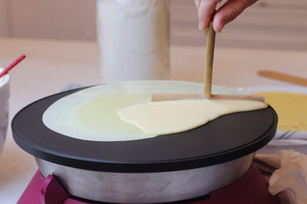 Thin crêpe batter being spread on a specialized electric crepe maker, capturing a classic French cooking process at home, emphasizing French cuisine and authentic culinary experience.