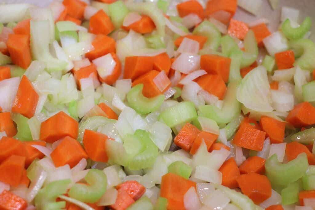 Freshly chopped celery, carrots, and onions for a rustic French vegetable sauté or soup. Bright orange, green, and white colors highlight fresh ingredients ideal for wholesome French cuisine.