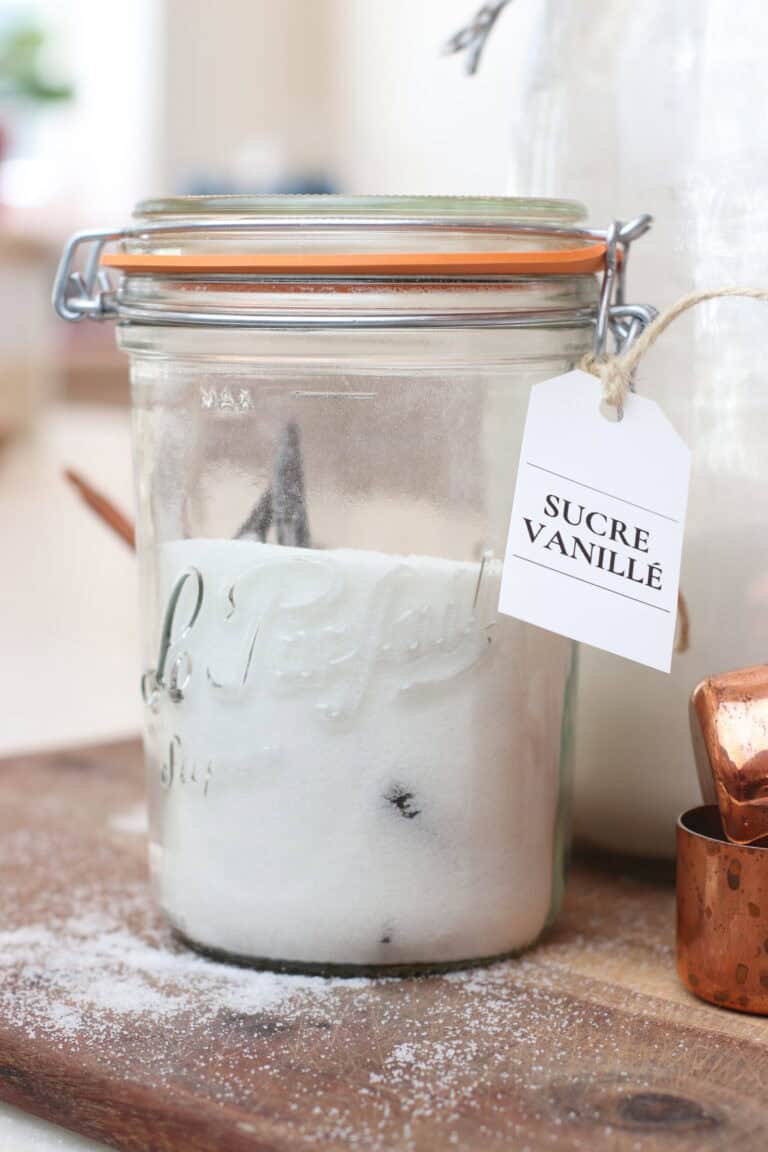 Glass jar of vanilla sugar labeled "Sucre Vanillé" with a vintage style, rustic kitchen setup, and baking ingredients.