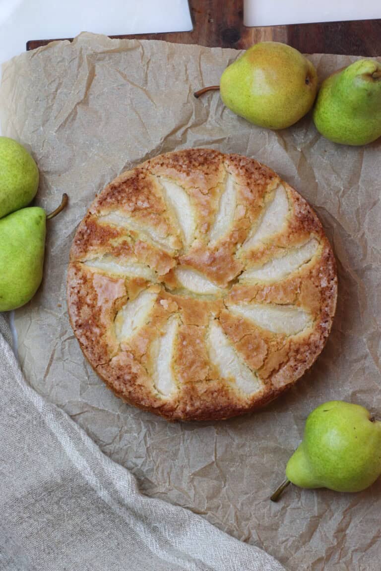 Golden pear cake on parchment paper, surrounded by fresh green pears, showcasing classic French pastry and rustic elegance.