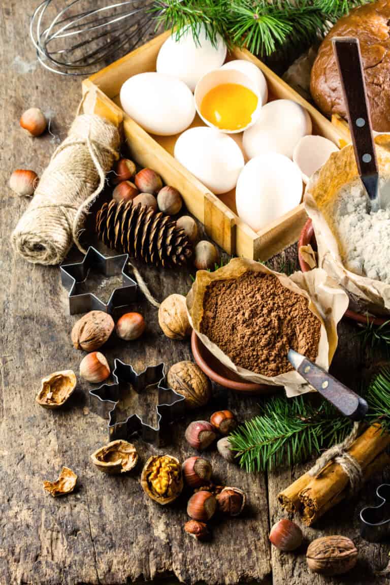 Eggs, nuts, flour, cocoa, and baking tools on rustic wooden table for holiday baking.